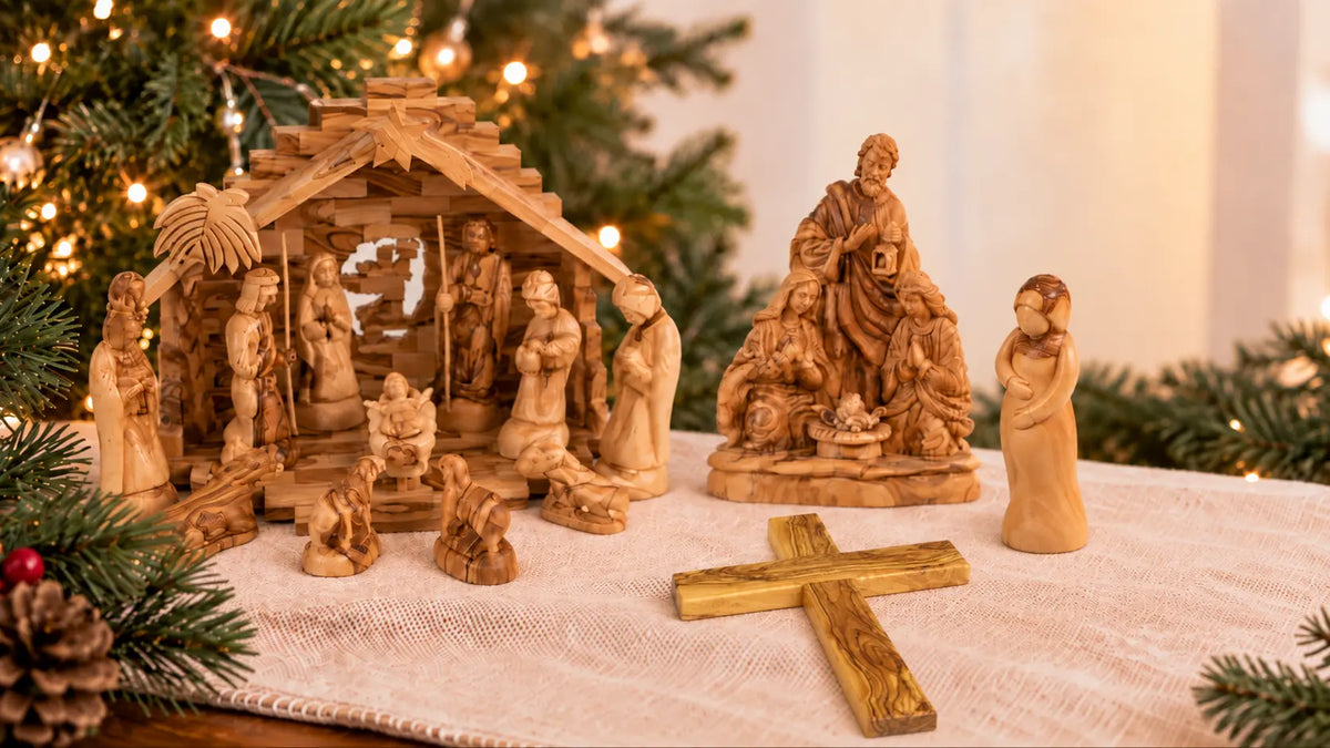 Olive wood Nativity sets, Christmas figurines, and wooden cross displayed beside a decorated Christmas tree.