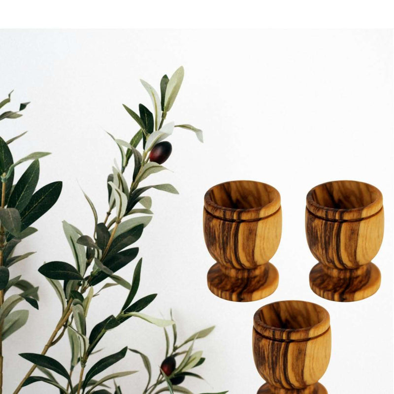 Three olive wood communion cups grouped beside an olive branch