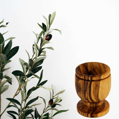 Single olive wood communion cup beside an olive branch on white #count_1 cup